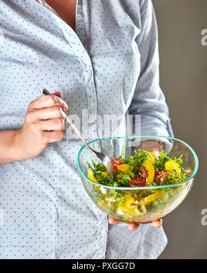 Mädchen Hände halten Schüssel mit Salat mit Käse und Gabel auf einem dunklen Hintergrund. Gesunde Snack Stockfoto