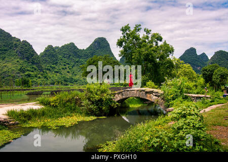 Mädchen im roten Kleid stand in der alten steinernen Brücke in Yangshuo Stockfoto