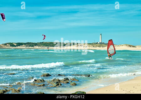 Menschen surfen vor dem Leuchtturm von Trafalgar, am Strand von Conil de la Frontera Spanien Stockfoto