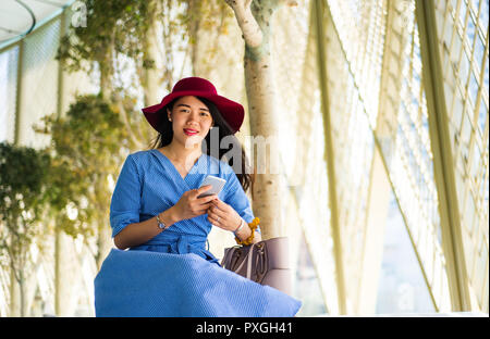 Modische asiatische Mädchen mit Telefon auf einem Balkon im Freien Stockfoto