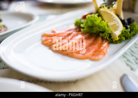 Scheiben geräucherter Lachs mit Zitronenscheiben auf weiße Platte serviert. Stockfoto