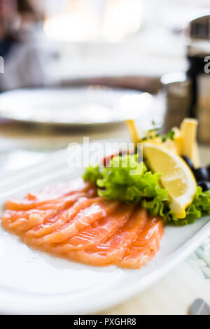 Scheiben geräucherter Lachs mit Zitronenscheiben auf weiße Platte serviert. Stockfoto