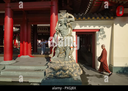 Ein buddhistischer Mönch in die Buddha Zahns Tempel & Museum, Singapur, als Besucher aus dem Main Gate verlässt, von einem Erziehungsberechtigten statue übersehen Stockfoto