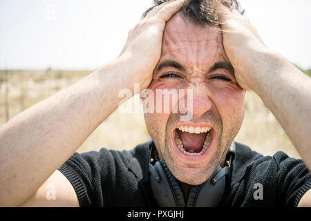 Sehr gefühlvoller junger Mann schreien und seinen Kopf Holding Stockfoto