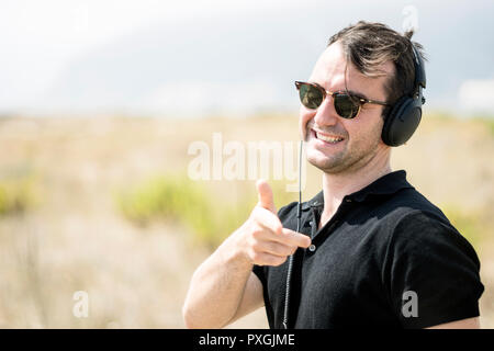 Jungen attraktiven Mann mit Sonnenbrille und Kopfhörer in die Kamera zeigen Stockfoto