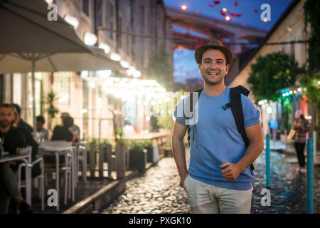 Glückliche junge Mann im blauen Hemd zu Fuß auf belebte Straßen mit Restaurants am evevning Stockfoto