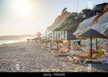 Bunte Sonnenliegen unter Stroh Sonnenschirme am Strand Praia da Falésia, Albufeira, Algarve, Portugal Stockfoto