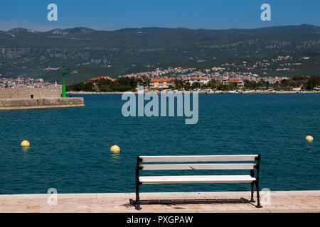 Sitzbank an der Küste des Bucht der Adria. Die Häuser auf der anderen Seite. Die Berge im Hintergrund. Blue Sky. Silo, Insel Krk, Kroatien. Stockfoto