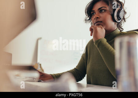 Portrait von Frau mit Kopfhörern am Computer Monitor suchen. Weibliche Programmierer an Ihrem Schreibtisch arbeiten. Stockfoto
