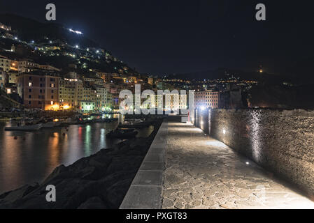 Einsame Stein Hafenpromenade in der Nacht in Camogli, Italien mit Reflexionen des Lichts von der Stadt auf dem Wasser mit angelegten Boote auf einem s Stockfoto