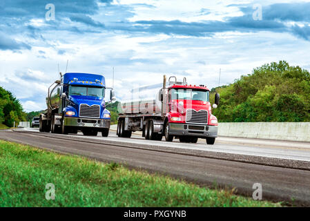 Horizontale Schuß von zwei Benzin Tankwagen auf der Interstate. Man hat ein rotes Cab und der Andere einen blauen Kabine. Bewölkter Himmel. Stockfoto