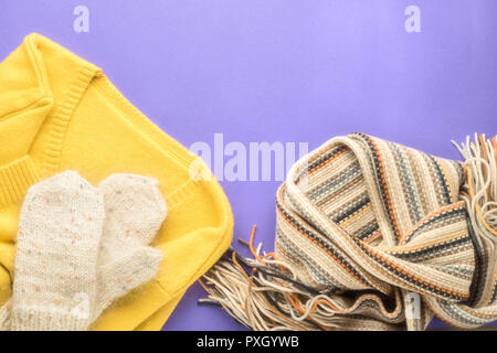 Herbst Winter Fashion saisonale Konzept pullover Strickjacke skandinavischen Strickschal und weißen flauschigen hausgemachte Handschuhe Fallen auf Papier lila Hintergrund F Stockfoto