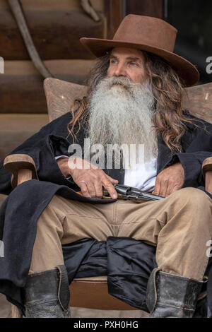 Den westlichen Menschen in der traditionellen Kleidung mit einem Colt 45 Sitzen auf einem Blockhaus Veranda Stockfoto