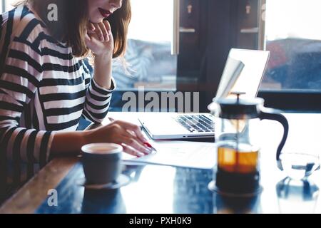 Bei der Arbeit konzentriert. Selbstbewussten jungen Frau in Smart Casual Wear Arbeiten am Laptop, während in der Nähe der Fenster in kreative Büro oder Cafe sitzen. Stockfoto