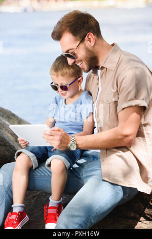 Vater und Sohn mit Tablet in der Nähe des Flusses im Park Stockfoto