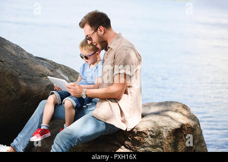 Vater und Sohn mit Tablet in der Nähe von See im Park Stockfoto