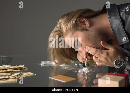 Seitenansicht des Drogenabhängigen jungen Mann Kokainschnupfen aus Glas Tisch Stockfoto