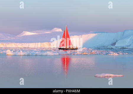 Kleine rote Segelboot Kreuzfahrt unter schwimmende Eisberge in der Diskobucht Gletscher mitternachtssonne Saison von polaren Sommer. Ilulissat, Grönland. Stockfoto