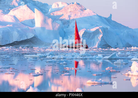 Kleine rote Segelboot Kreuzfahrt unter schwimmende Eisberge in der Diskobucht Gletscher mitternachtssonne Saison von polaren Sommer. Ilulissat, Grönland. Stockfoto