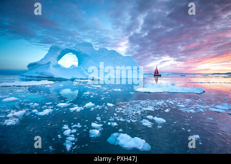 Kleine rote Segelboot Kreuzfahrt unter schwimmende Eisberge in der Diskobucht Gletscher mitternachtssonne Saison von polaren Sommer. Ilulissat, Grönland. Stockfoto