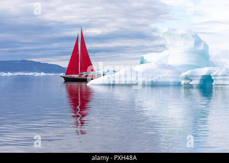 Kleine rote Segelboot Kreuzfahrt unter schwimmende Eisberge in der Diskobucht Gletscher mitternachtssonne Saison von polaren Sommer. Ilulissat, Grönland. Stockfoto