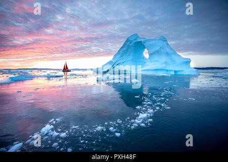 Kleine rote Segelboot Kreuzfahrt unter schwimmende Eisberge in der Diskobucht Gletscher mitternachtssonne Saison von polaren Sommer. Ilulissat, Grönland. Stockfoto