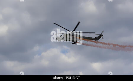 Kampfhubschrauber mit roten Rauch auf blauer Himmel mit weißen Wolken. Ansicht von unten. Stockfoto