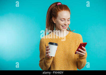 Junge rothaarige Frau mit Kaffee und Smartphone über b isoliert Stockfoto