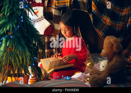 Frohe Weihnachten und schöne Feiertage. Das glückliche Mädchen ein Buch lesen im Winter zu Hause. Das Holiday, Kindheit, Winter, Feier Konzept Stockfoto