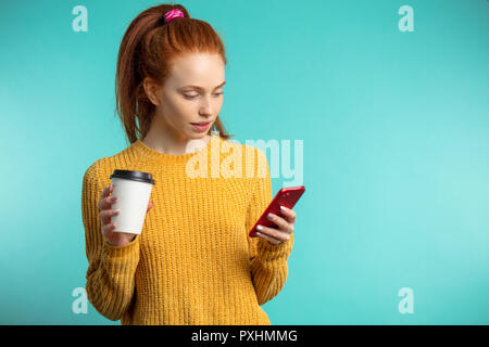 Junge rothaarige Frau mit Kaffee und Smartphone über b isoliert Stockfoto