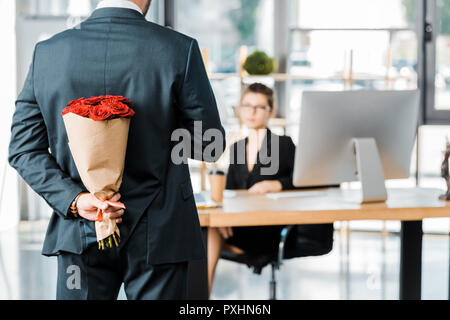 Zugeschnittenes Bild des Geschäftsmannes ausblenden Blumenstrauß aus Rosen hinter Zurück zur geschäftsfrau Überraschung im Büro Stockfoto