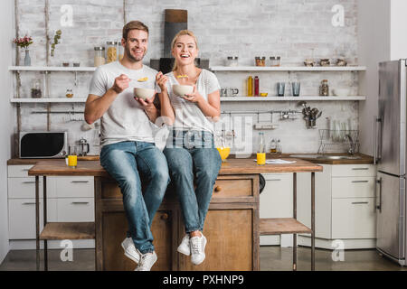 Glückliches Paar, das Frühstück und das Sitzen auf den Küchentisch Stockfoto
