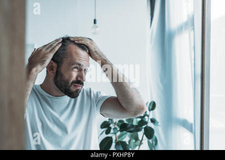 Umgekippt im mittleren Alter Mann mit Alopezie im Spiegel zu betrachten, Haarausfall Konzept Stockfoto