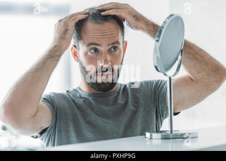 Mitte der erwachsene Mann mit Alopezie bei Spiegel bärtigen, Haarausfall Konzept Stockfoto