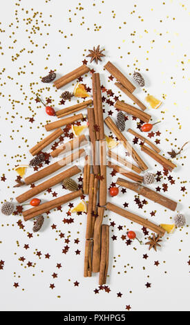 Weihnachtsbaum aus Zimtstangen, Kegel, Orangen, glänzende Sterne und präsentiert. Weißer Hintergrund, Ansicht von oben, flach Stockfoto