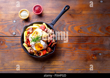 Chilenischen essen. CHORRILLANA - Pommes frites garniert mit Rindfleisch in Scheiben geschnitten, typische Wurstwaren chorrisos, gebratenen Zwiebeln und Eier in Gusseisen Pfanne mit Saucen serviert. Stockfoto