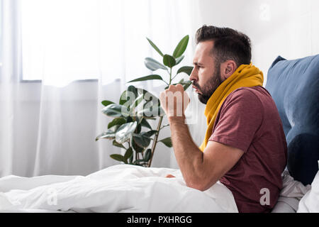 Seitenansicht des Kranken jungen Mann in Husten während Sie im Bett sitzen Stockfoto