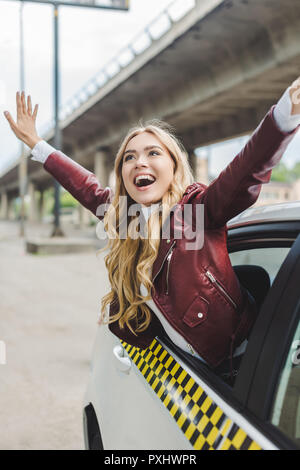 Fröhliche blonde Mädchen die Hände und Wegsehen durch taxi Fenster Stockfoto