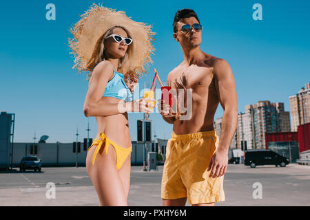Schöne junge Paar in Strand Kleidung mit erfrischenden Cocktails stehen auf Parkplatz Stockfoto