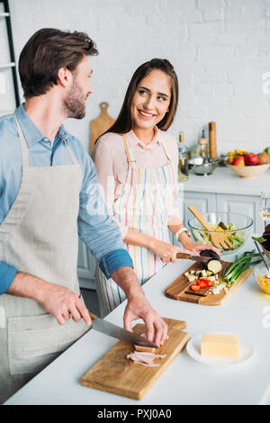 Lächelndes Paar kochen und Schneiden von Gemüse mit Fleisch in der Küche Stockfoto