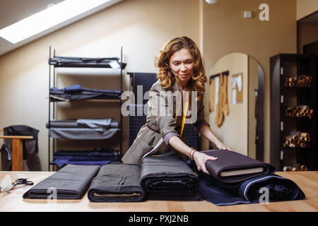 Weibliche maßgeschneiderte Auswahl Gewebe für Schnitttechnik. Männer der Industrie tragen, Schneiderei Prozesskonzept Stockfoto