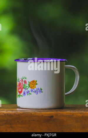 Weiß Emaille Tasse heißen dampfenden Kaffee sitzen auf Holz Eisenbahn durch einen Regenwald. Flache Tiefenschärfe mit selektiven Fokus auf Tasse. Stockfoto