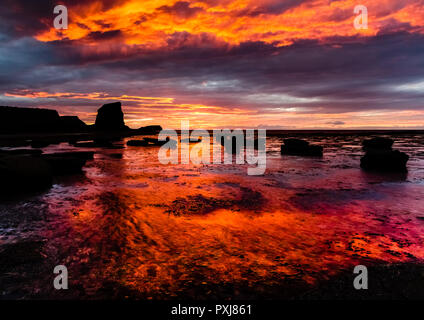 Ein dramatischer Sonnenuntergang über schwarzen Nab und Saltwick Bay dreht sich im seichten Wasser rot, wie die Sonne über der Nordsee setzt Stockfoto