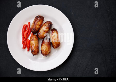 Traditionelle thailändische Essen. Gegrillte Wurst aus Schweinefleisch mit roten Chilis auf weiße Platte auf schwarzer Holztisch. Stockfoto