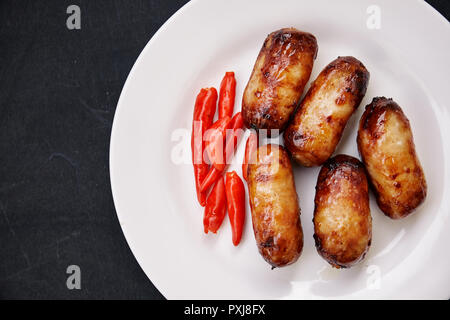 Ansicht von oben, in der Nähe von gegrilltem Schweinefleisch Wurst und rote Chilis auf weiße Platte. Thailändisches Essen. Stockfoto