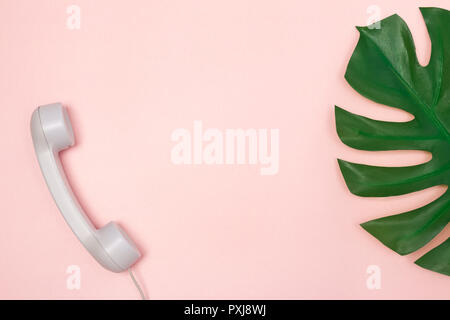 Traditionelles Telefon Empfänger und Monstera palm leaf auf Pastell rosa Hintergrund, mit kopieren. Stockfoto