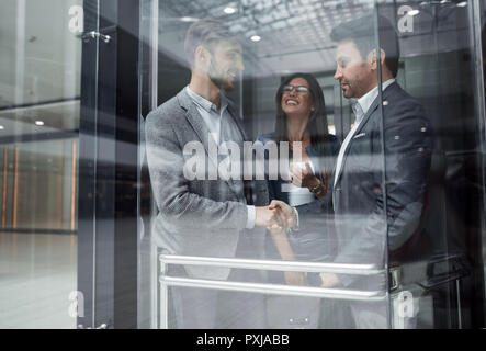 Kolleginnen und Kollegen die Hände schütteln im Fahrstuhl. Business Konzept Stockfoto