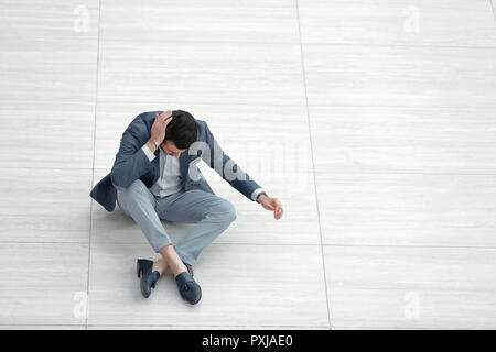 Frustrierte junge Unternehmer sitzen auf dem Boden und blickte nach unten. geschäftliche Problem Konzept Stockfoto