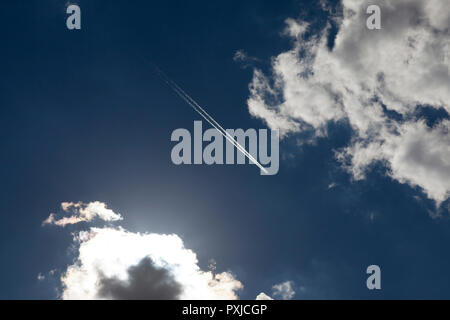 Fliegen hoch in den Himmel Flugzeug, hinter denen es eine Umkehr weg aus dem Motor, vor dem Hintergrund eines blauen Himmel und weiße Cumulus cloud Stockfoto