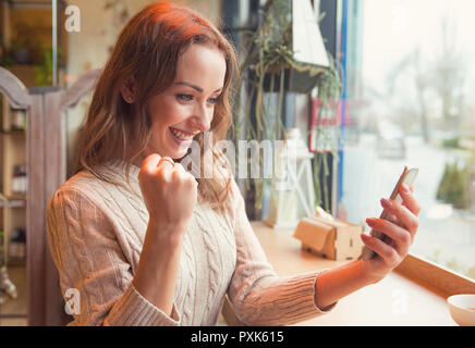 Euphorisch super aufgeregt Frau gerade Ihre Smart Phone, während im Cafe sitzen Stockfoto